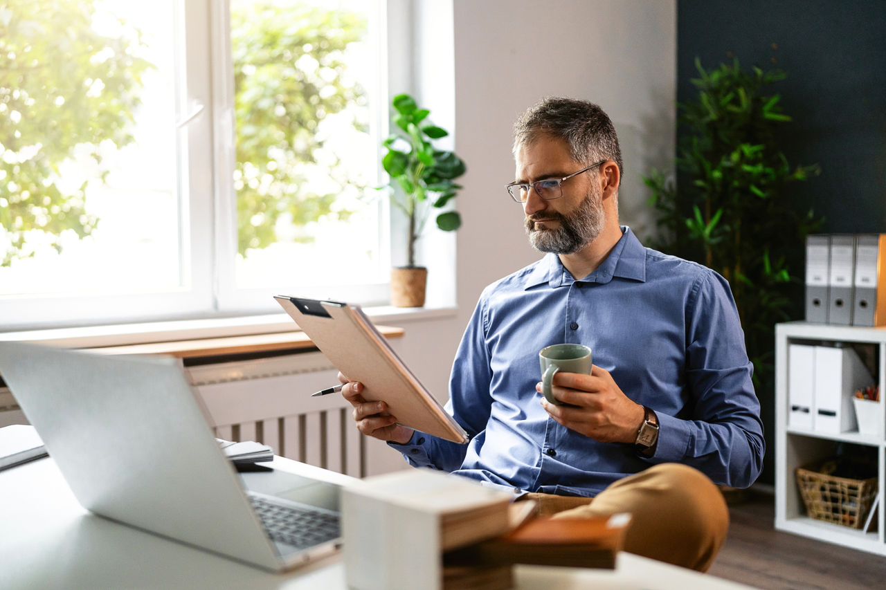 Mid-adult Caucasian businessman, drinking coffee while working at the modern office