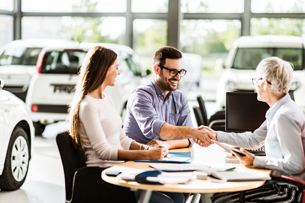 Happy couple came to an agreement with car salesperson on a meeting in a showroom. Focus is on man.