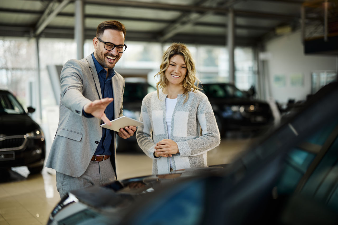 Happy car salesman showing a car to his customer in a showroom.