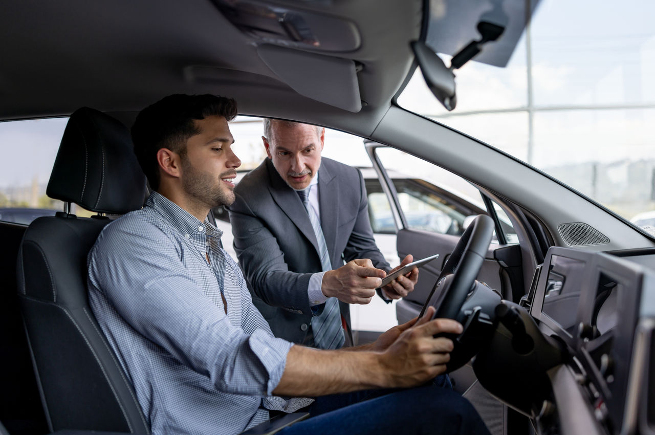 Salesman showing the interior of a car to a man interested in buying a vehicle - car dealership concepts