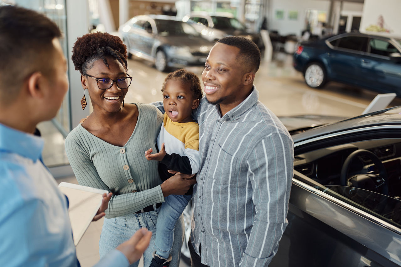 Happy African American family communicating with male salesperson in a car showroom.