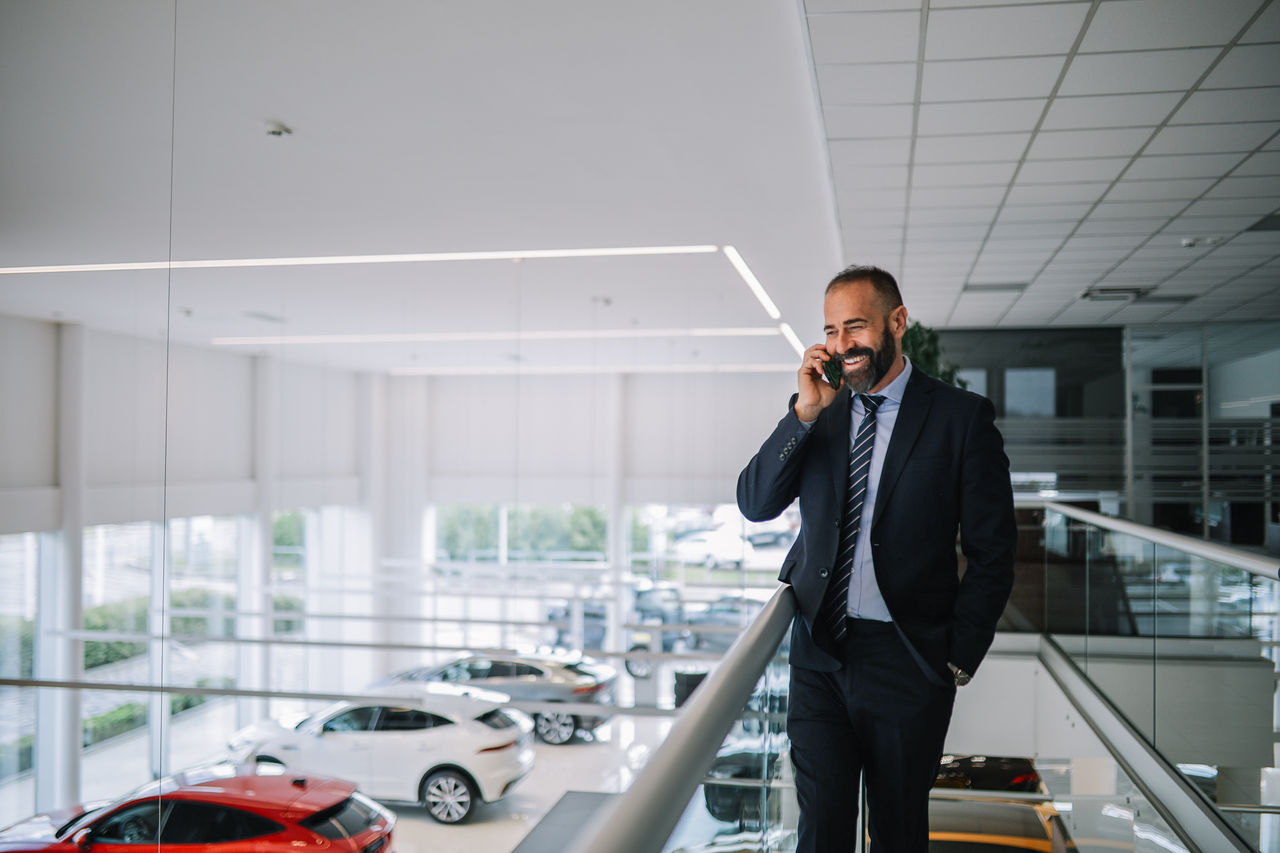 Mid aged man working in the luxury car showroom - dealership. He is checking his mobile phone, answering calls and emails, going through everyday stuff.