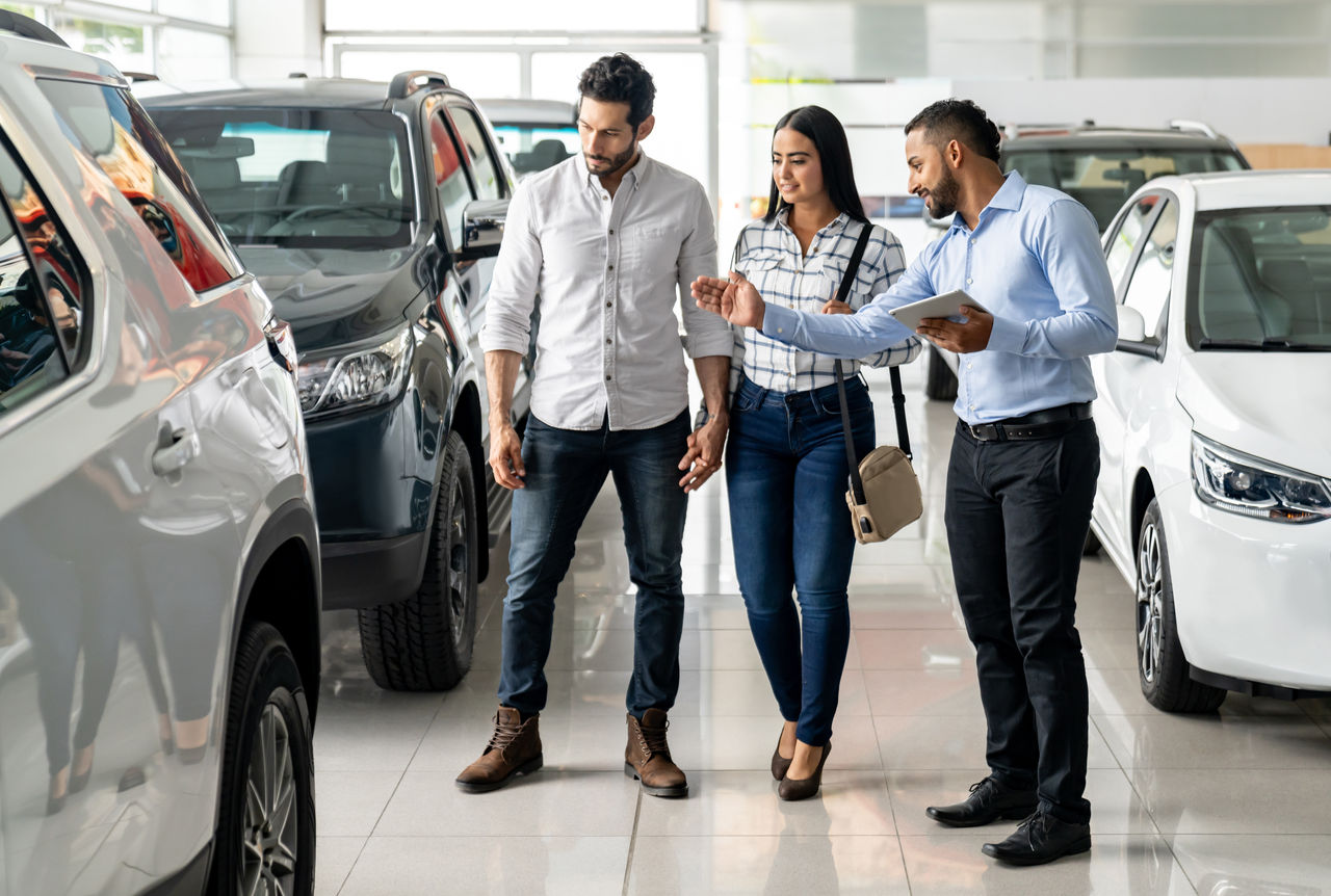 Latin American salesman at the dealership showing a car to a couple interested in buying a vehicle - business concepts