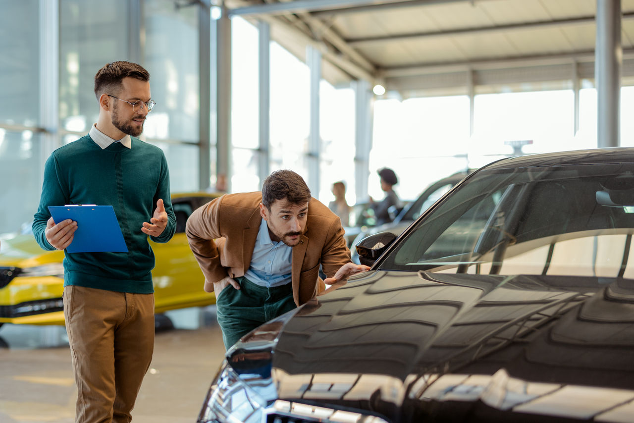 Car Salesman Showing a Car to His Male Customer in a Dealership Office