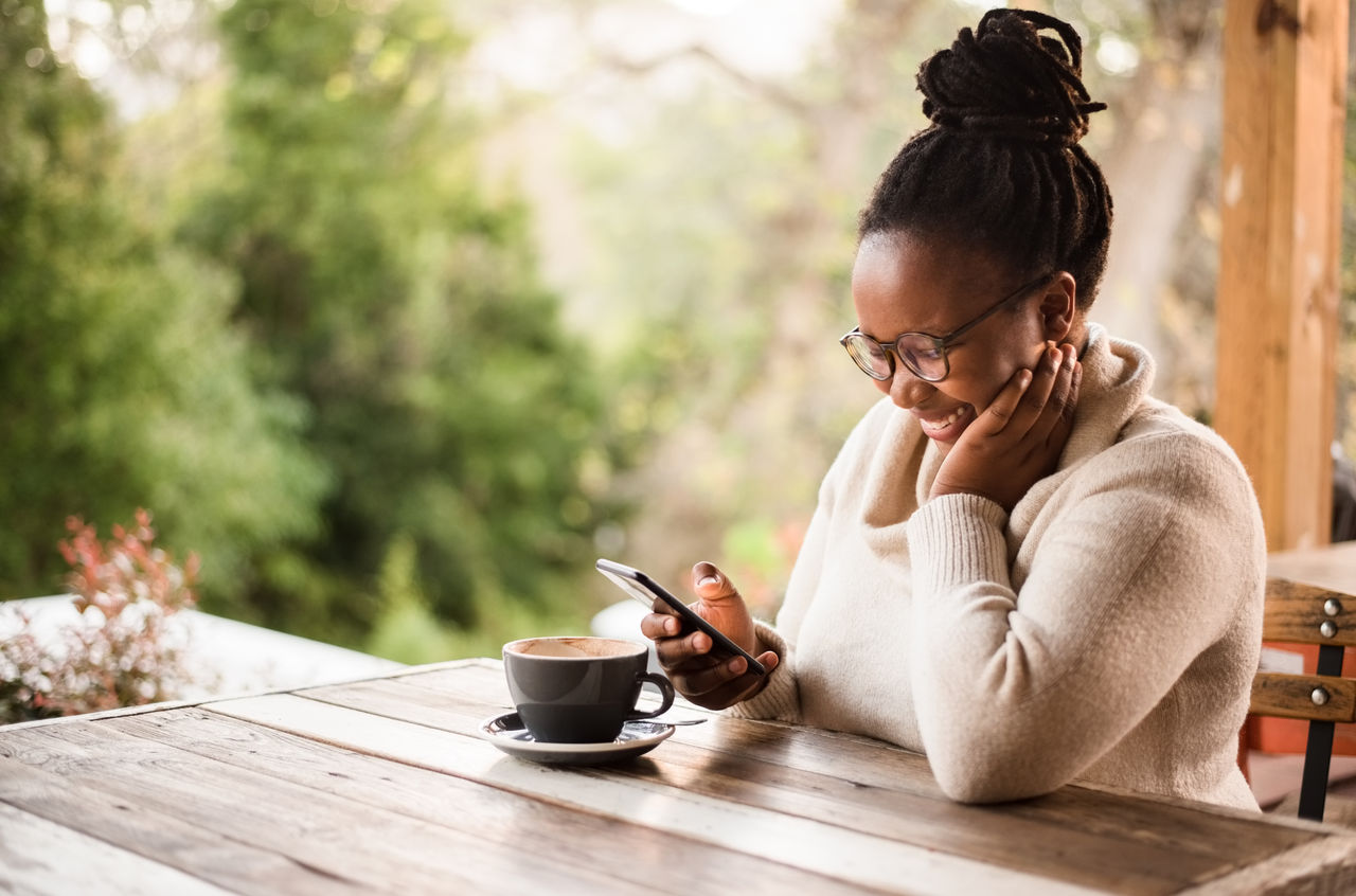 Shot of a young african woman reading text message on mobile phone and smiling while sitting in a coffee shop