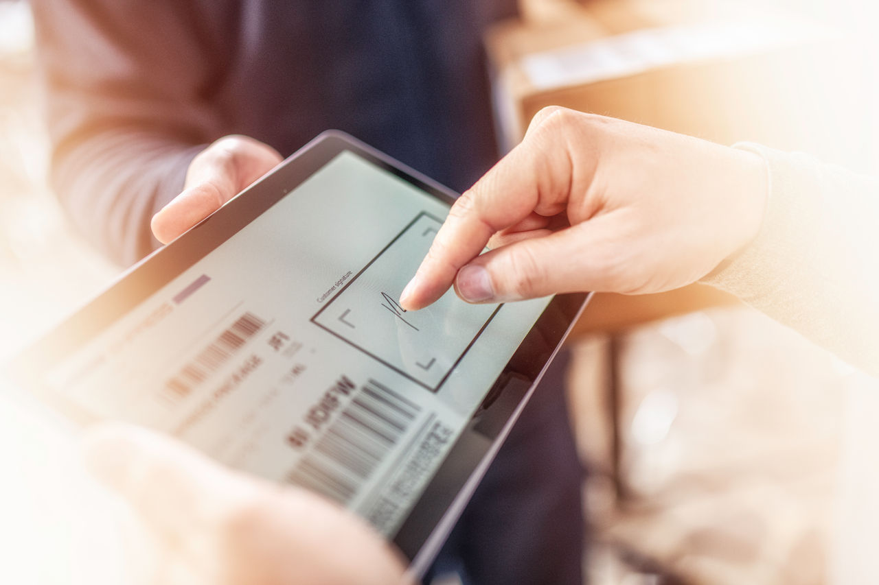 Courier holding package and tablet while male customer is signing receipt for his home delivery parcel.