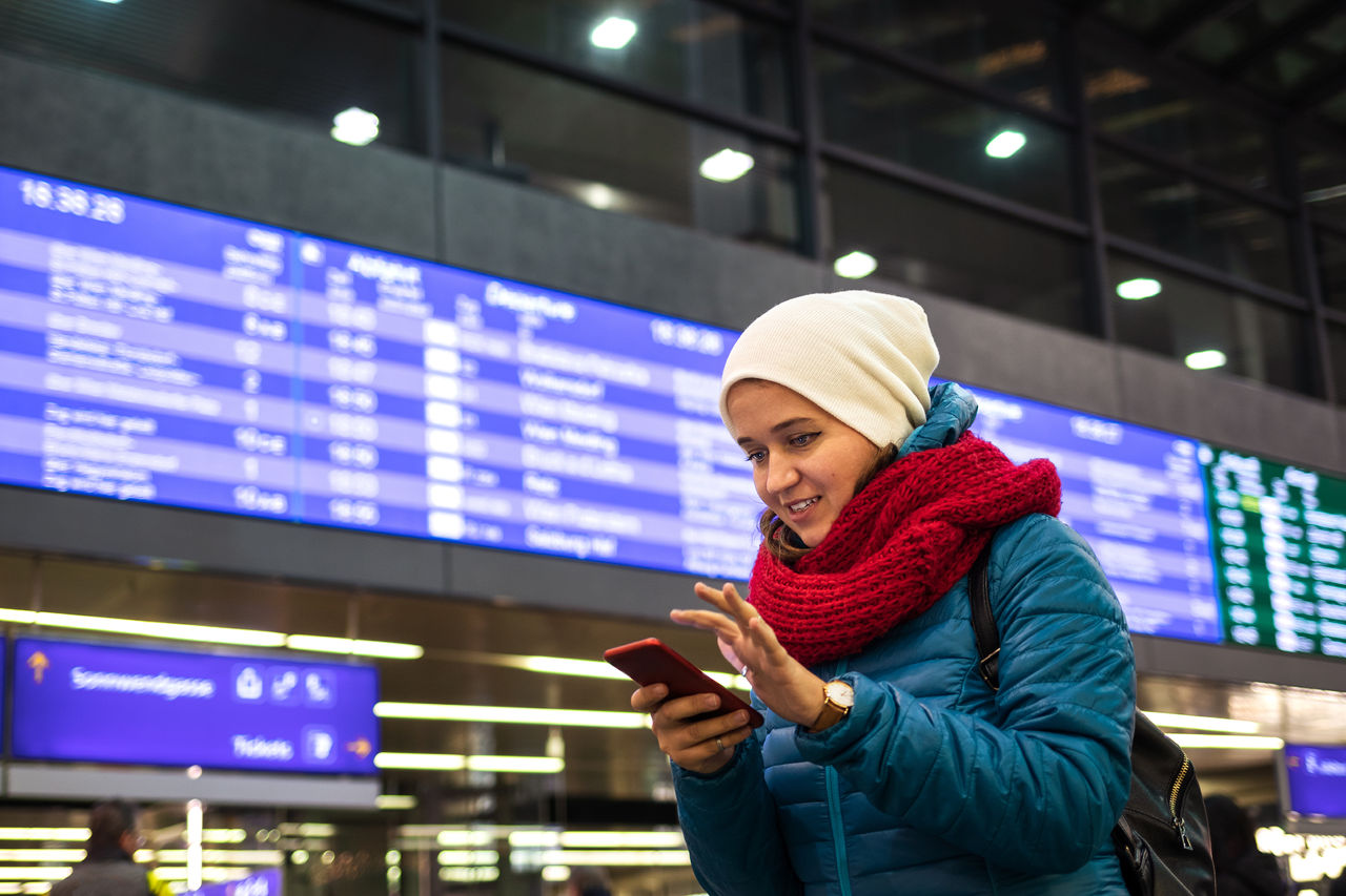 Tourist is standing under arrival departure board or timetable at railroad station