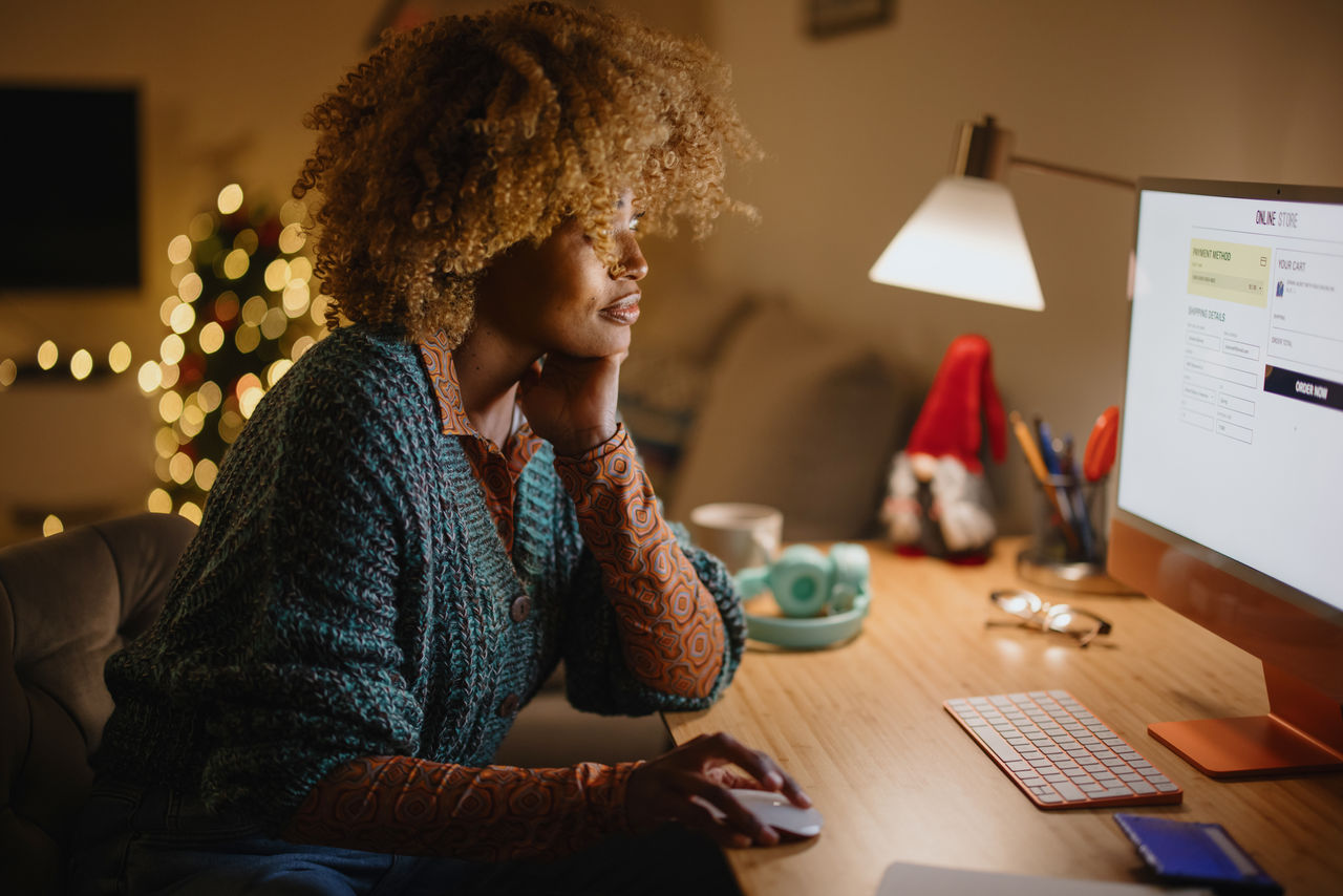Middle aged woman buying online Christmas presents from her cozy home late at night. Woman using PC computer for online Christmas shopping.