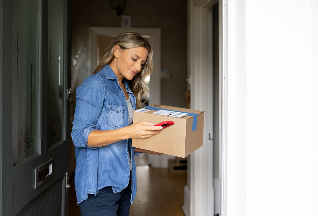 Happy woman receiving a package at home and getting a notification on her cell phone â   domestic life concepts