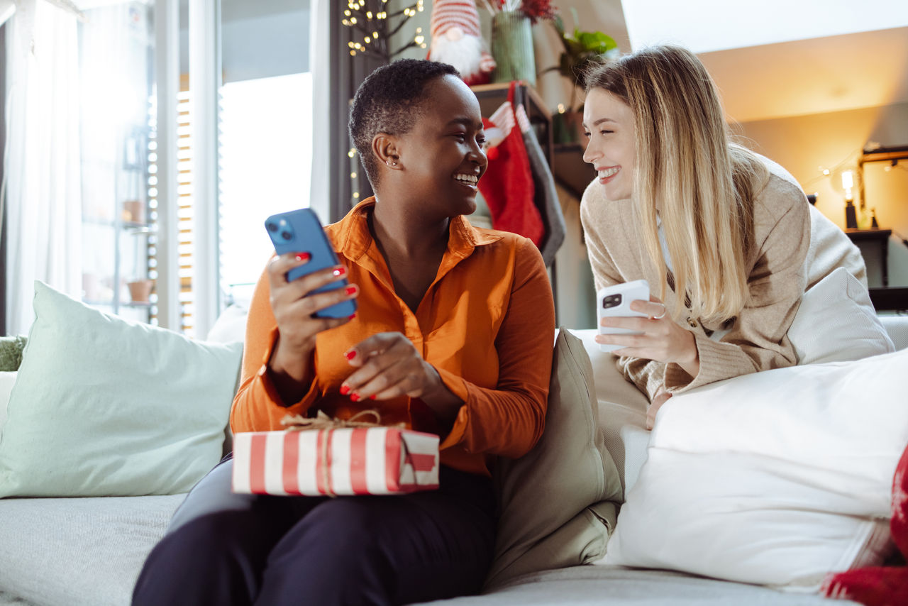 Two young women enjoying at home in the living room during Christmas time. They are smiling and talking
