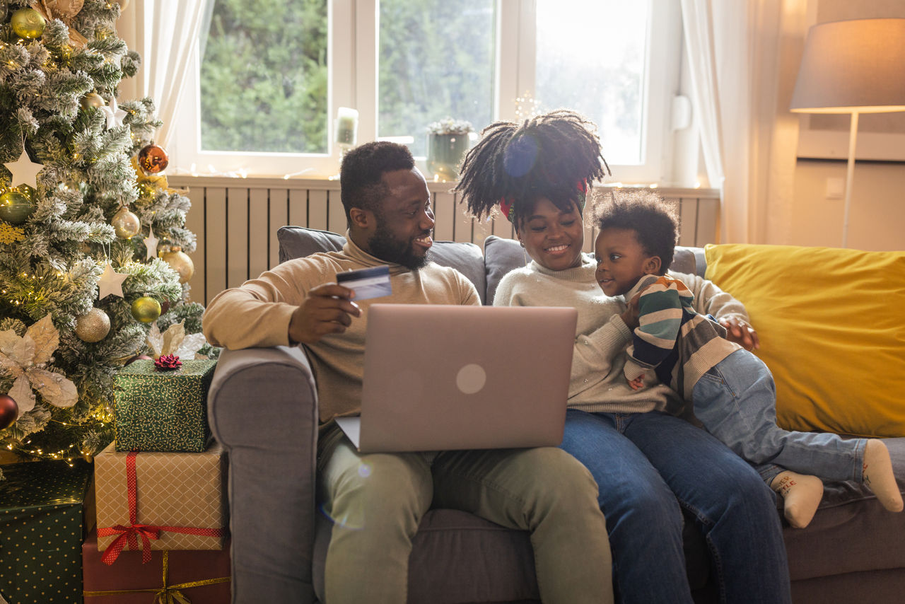 Young family celebrating Christmas at home. They are having fun and using laptop for online shopping..