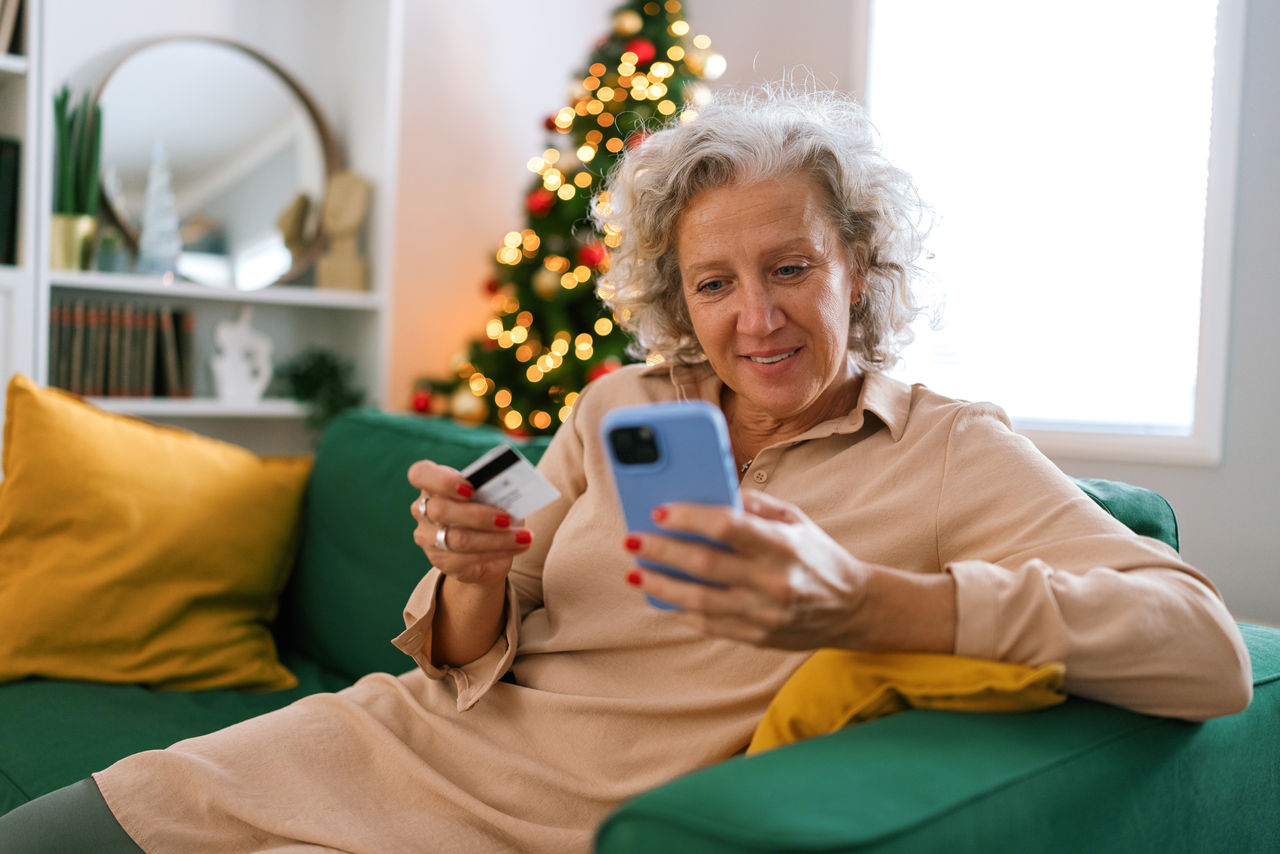 Middle-aged woman using credit card for Christmas shopping online