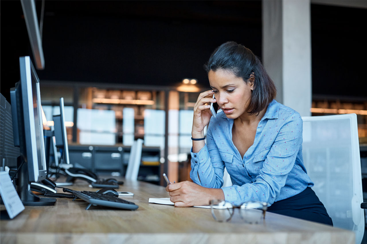 Young businesswoman using smart phone at desk. Female professional is sitting in textile factory. She is working in office.