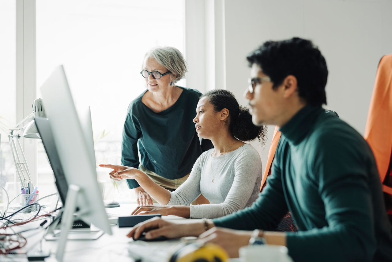 Female architects discussing a project looking at computer monitor with a male colleague working in front. Business people working together in an engineering office.