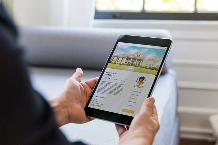 An unrecognizable man uses a real estate mobile app in his search for a new home. An exterior photo of the home is on digital tablet's screen.