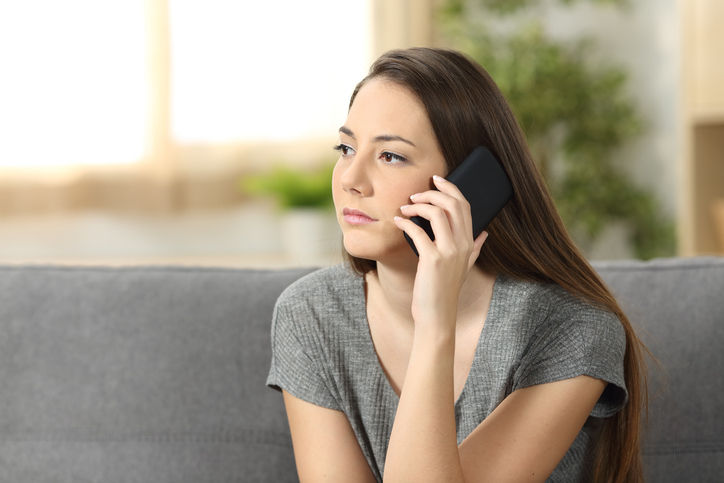 Serious woman attending a phone call sitting on a sofa in the living room at home