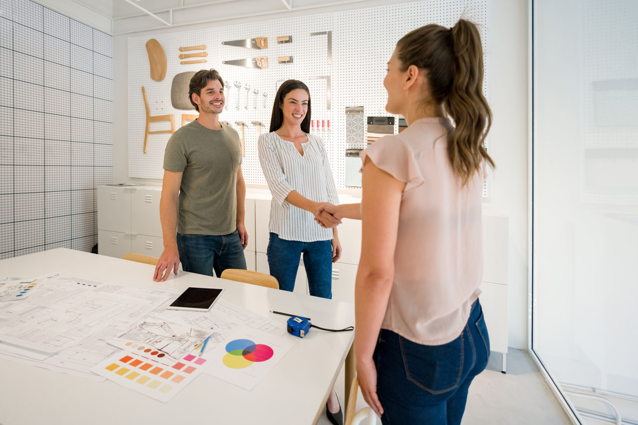 Happy architect closing a deal with her clients at the office with a handshake. **DESIGN OF DOCUMENTS ON TABLE BELONG TO US**