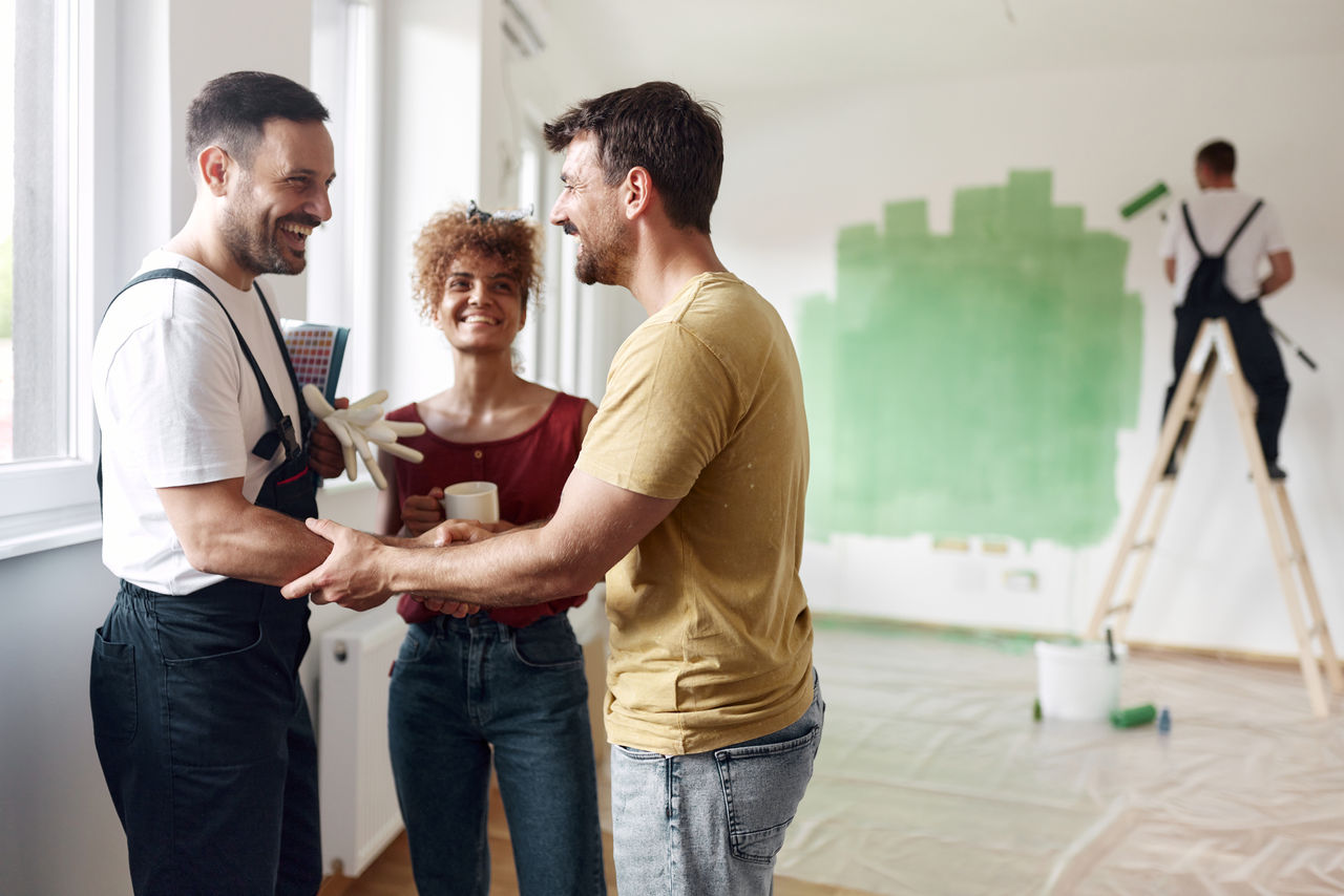 Happy couple came to an agreement with house painter at renovating apartment. Copy space.