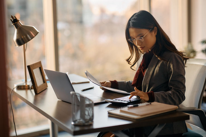 Asian businesswoman making calculations while going through reports and working in the office.