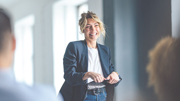 Beautiful cheerful woman in a dark blue jacket standing in front of a crowd looking down at a tablet.