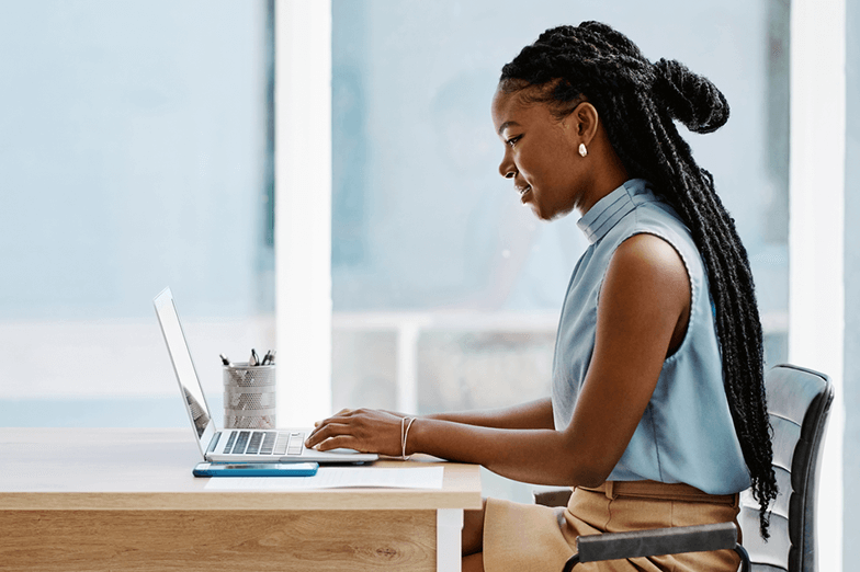 Woman in blue shirt sitting at desk typing on laptop