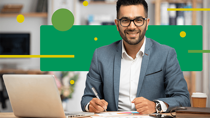 Man sitting at desk with laptop smiling with pen in hand