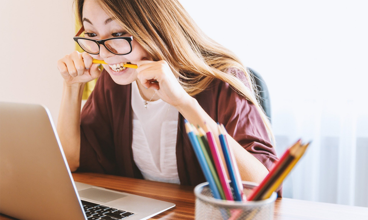 Stressed woman biting down on a pencil looking at a laptop