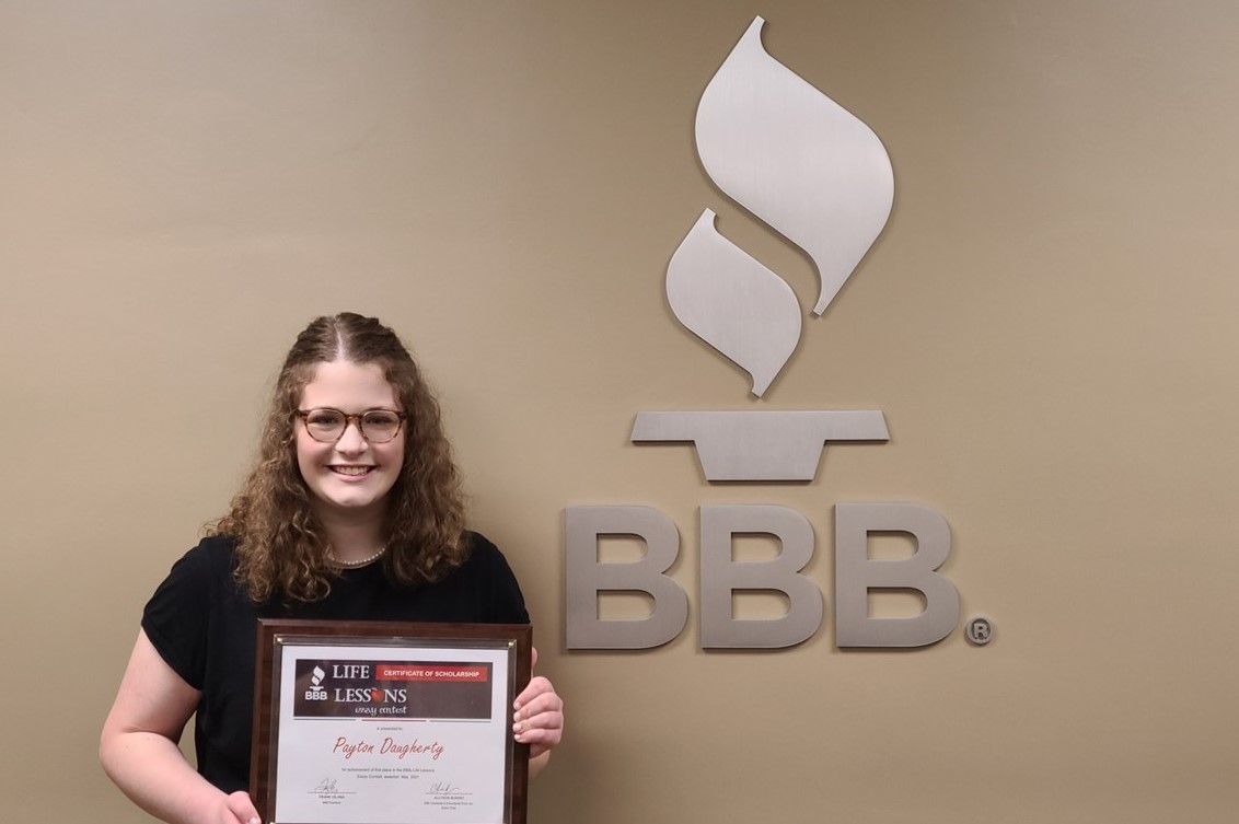 Essay winner Peyton Daugherty holding plaque next to BBB sign