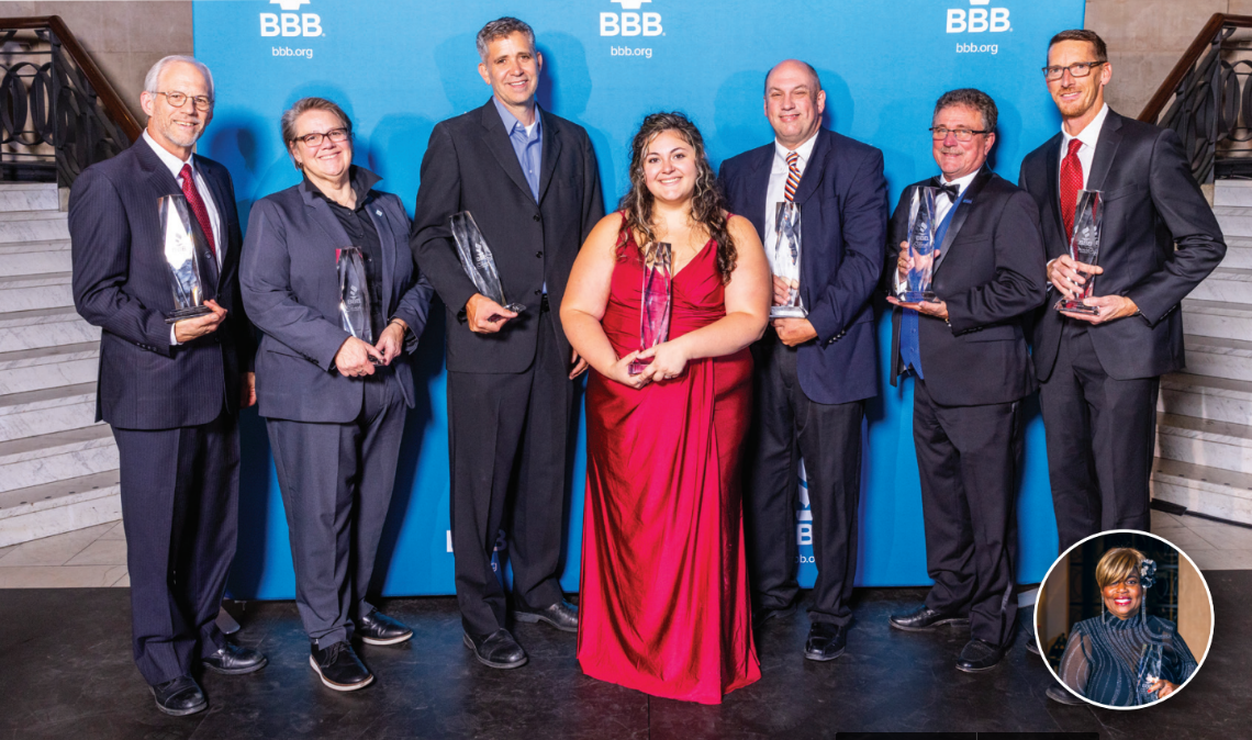 Seven 2023 Torch Awards for Ethics winners with trophies on a stage in front of a blue BBB backdrop.