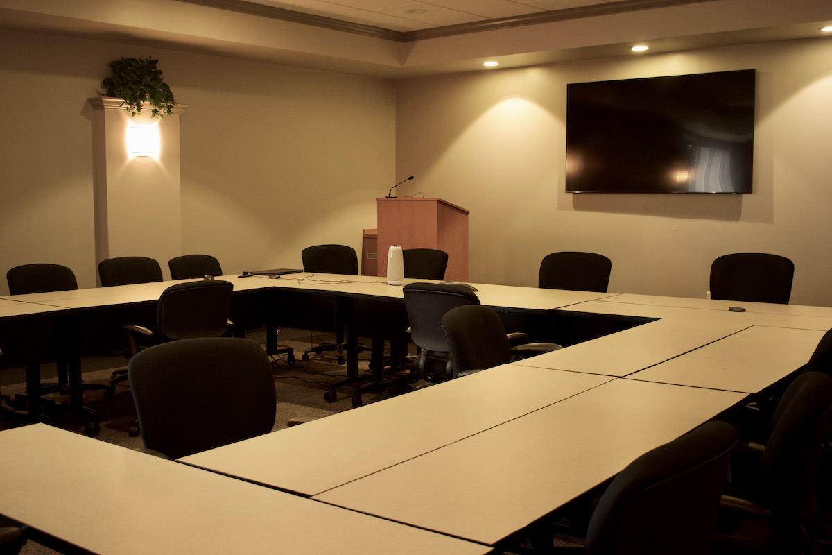 Alternate view of large board room; desks arranged in square formation with large TV on opposite wall
