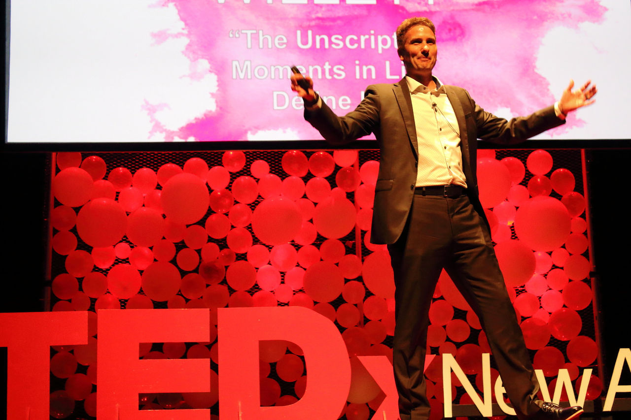Speaker with white shirt on stage with red TedX behind him