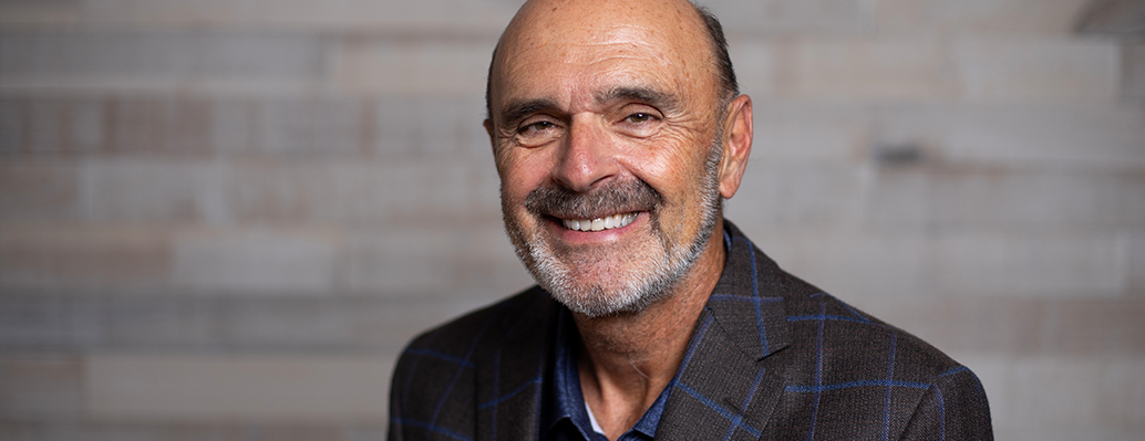 Smiling man with gray beard in front of a white brick wall