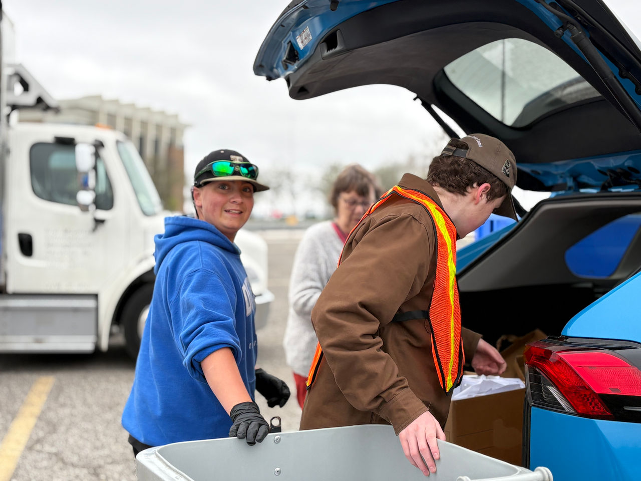Two smiling teenage boys emptying paper from the back of an SUV into a bin