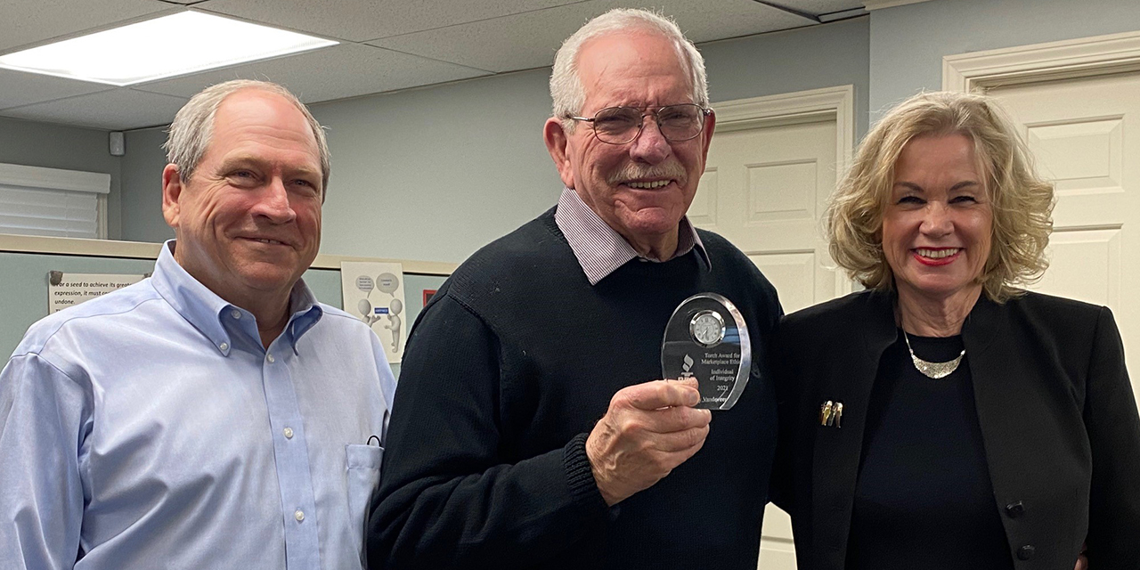 Smiling man in center accepts an award from man on left and woman on right