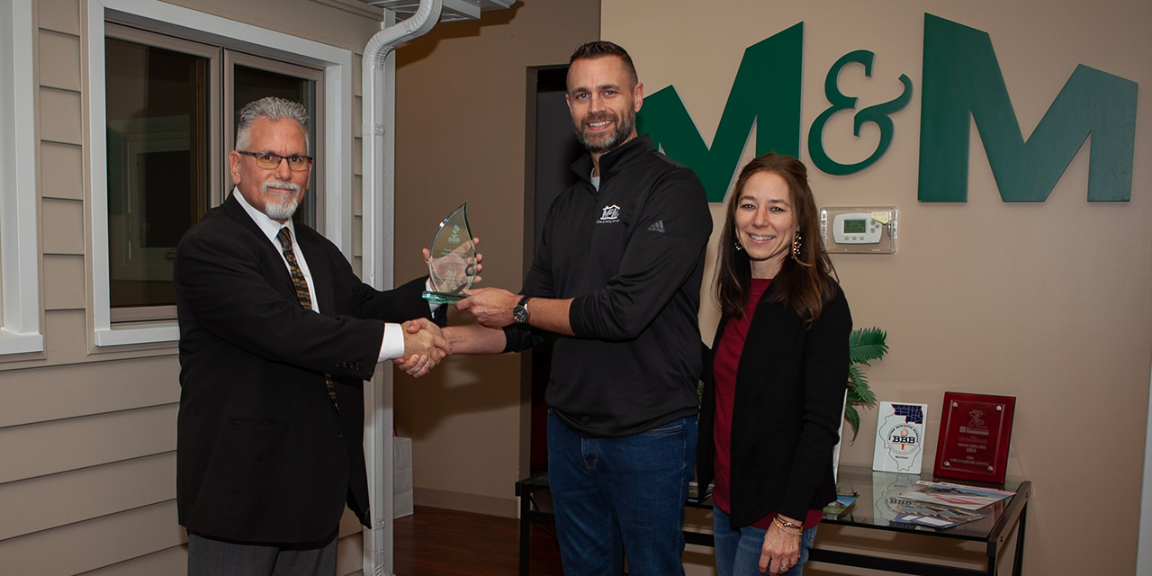 A man presenting an award to two employees, one male, one female