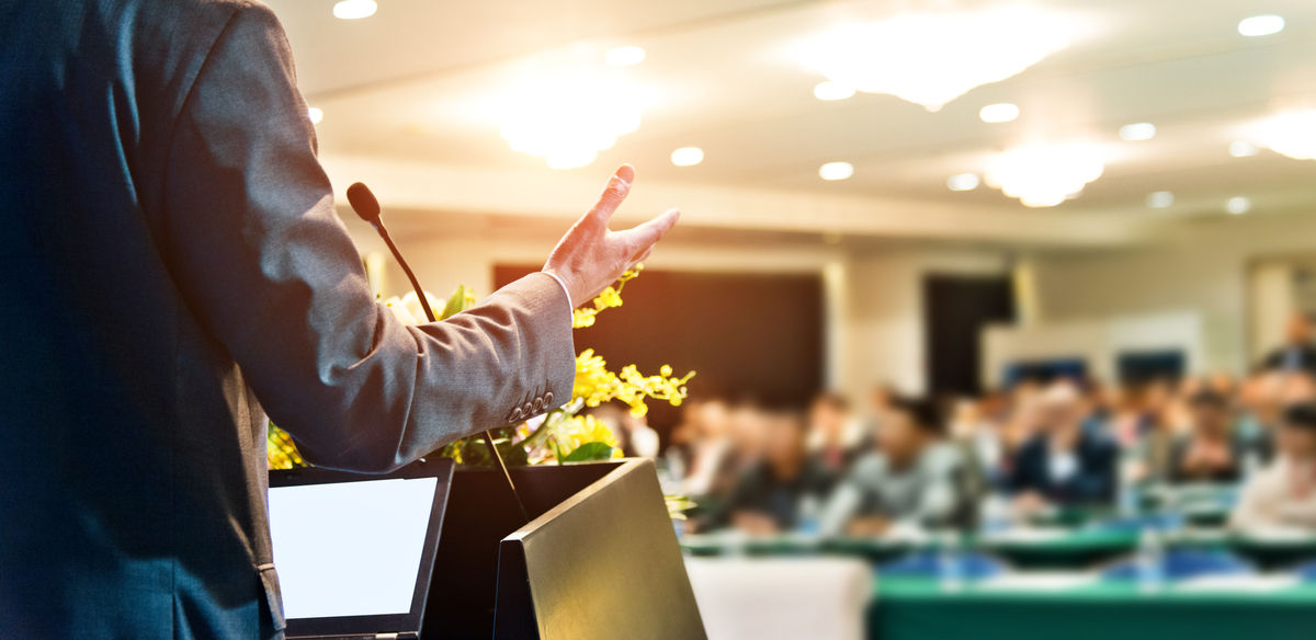 Unrecognizable businessman making a speech in front of audience at conference hall.