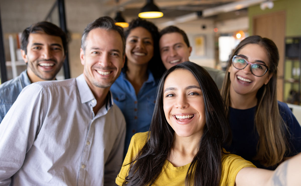 Happy group of Latin American coworkers taking a selfie at the office and looking at the camera smiling