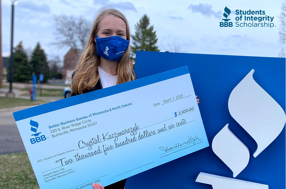 Student Crystal poses with a large check outdoors in front of large BBB sign