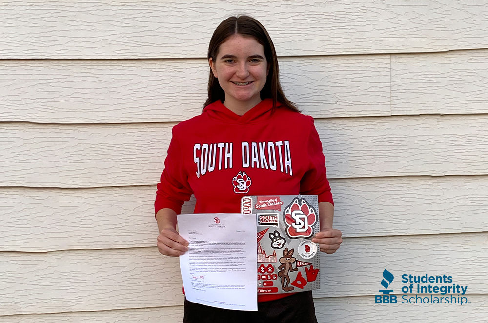 Student Kaitlyn Kirchner poses in a University of South Dakota sweatshirt, holding her admission packet.