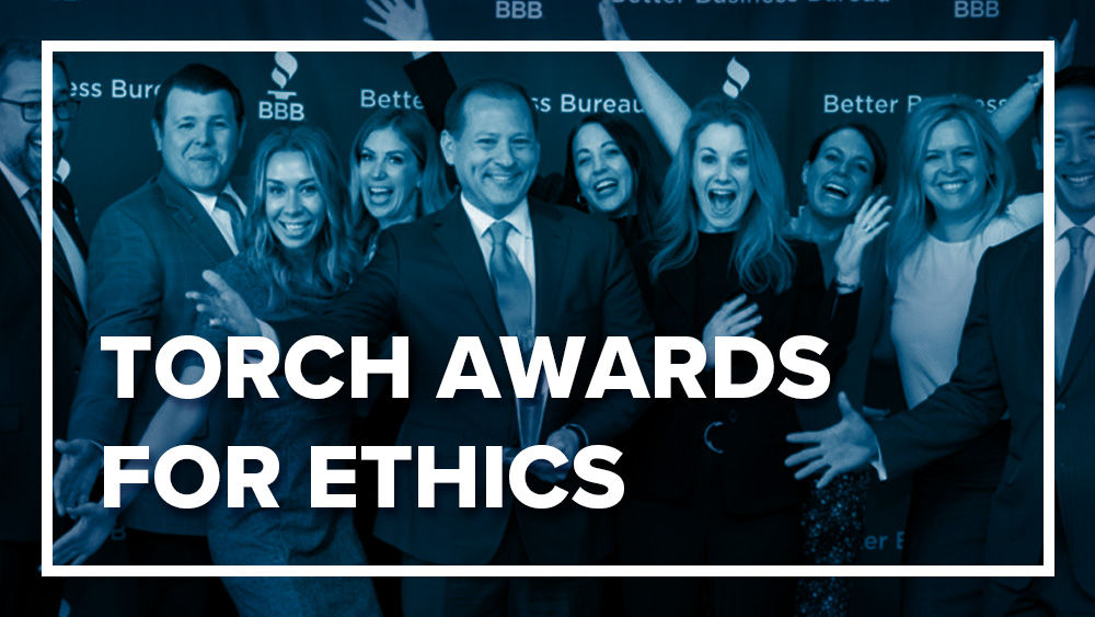 White text reading "Torch Awards for Ethics" inside white box over blued out image of team celebrating