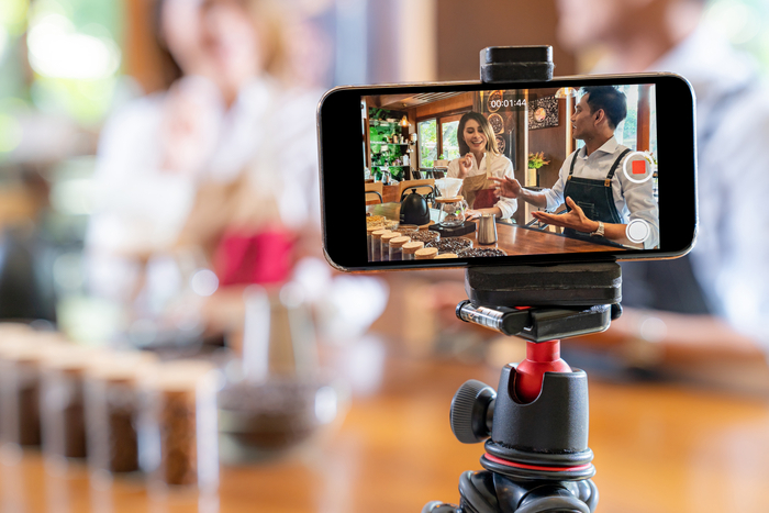 VLOG of  young adult asian owner entrepreneur review cafe coffee shop and live in social media for online marketing with smart phone in cafe. Using for startup of small business maketing and consumerism concept.