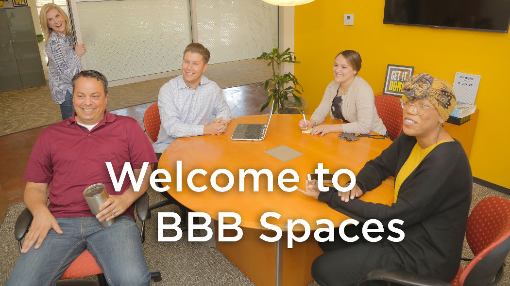 Group of business people sitting around a table smiling. Text says Welcome to BBB Spaces. 