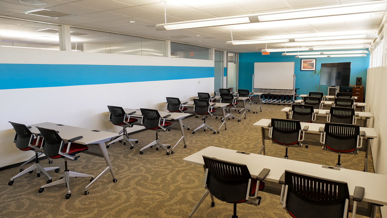 long room set up lecture style with a blue wall, white board, and large television screen at the the end of the room