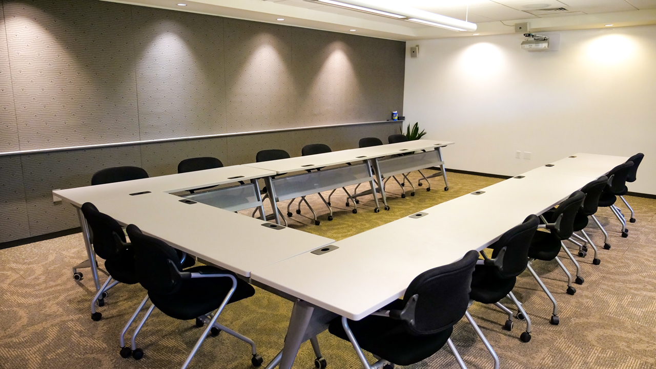room with a table set up in u-shape with chairs around the table, whiteboard wall at the end of the room