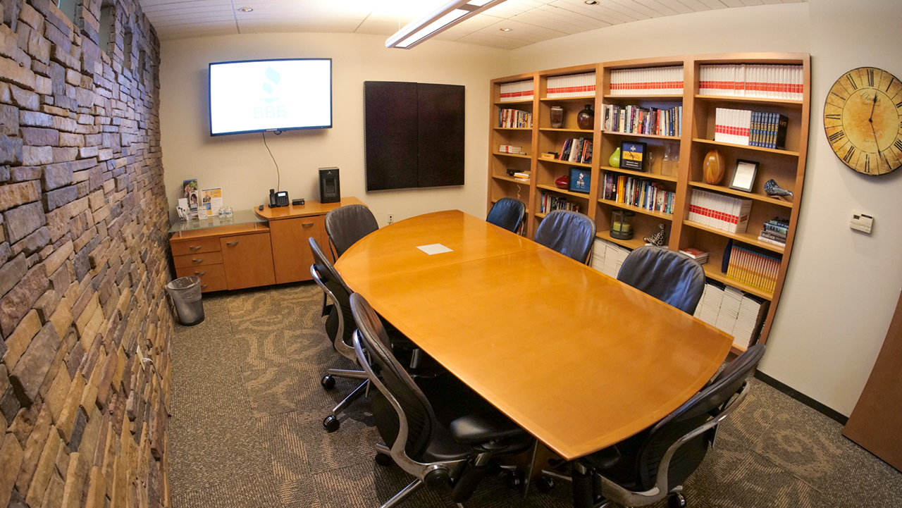 room with a rectangle table, television screen in the corner, and a large bookshelf full of books