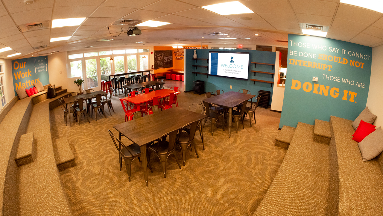 amphitheater type room with several dining tables in the middle, large television screen on the wall