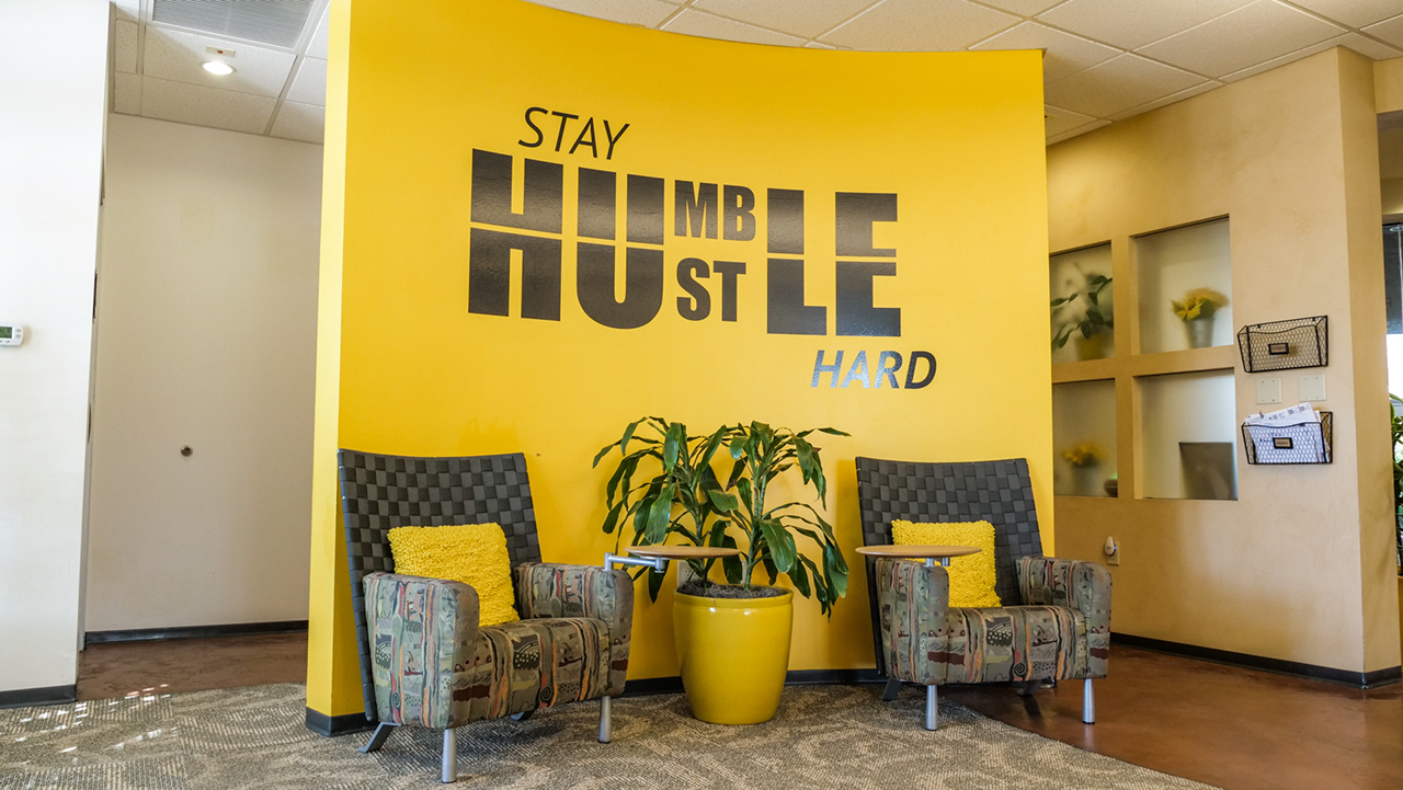 yellow wall with words reading hustle hard stay humble and two chairs 