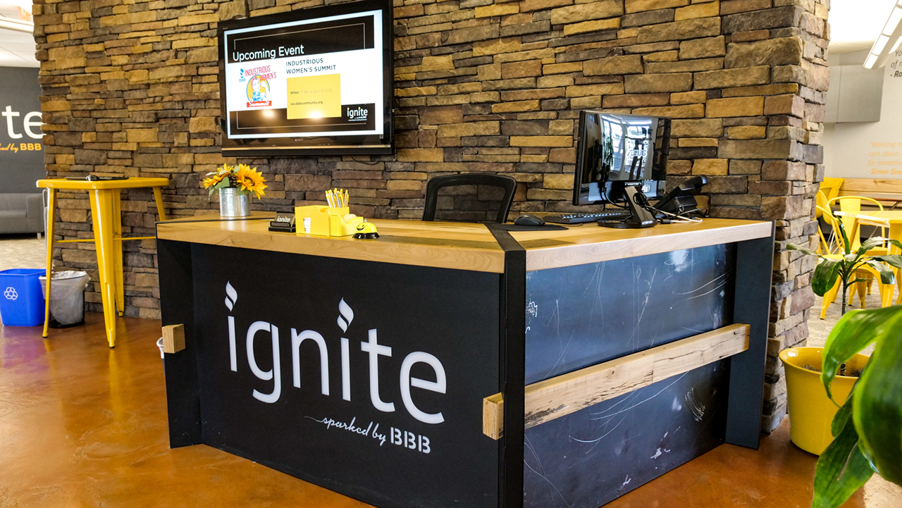 black industrial metal and wood front desk with words reading ignite sparked by BBB on the front and a tv in the bacakground