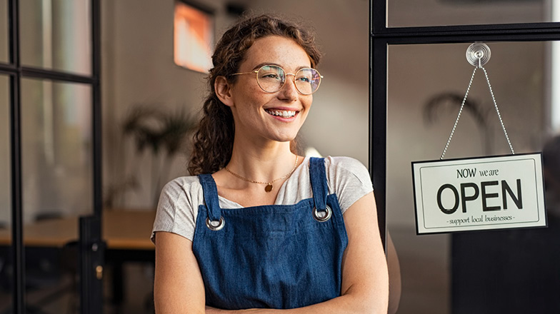 Female business owner standing in front of small business with "open" sign in the window