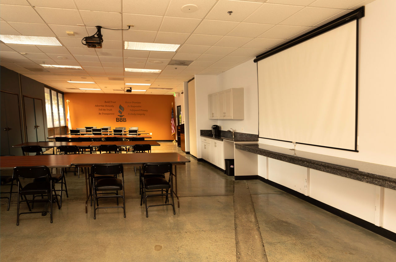 Large room with tables and chairs, with orange wall and BBB logo, Goggin conference room
